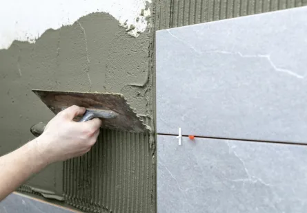 Tile adhesive being spread on a wall with a notched trowel